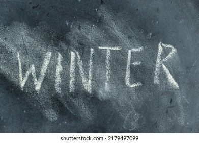 Semi-erased Word WINTER On Black Chalkboard. Handwritten Word. Fuzzy Letters On Black Surface. The Concept Of The Changing Seasons Of The Year.