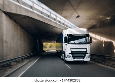 Semi-truck with cargo trailer driving at the tunnel. Fast moving truck. Lorry driver ride his modern truck under the bridge