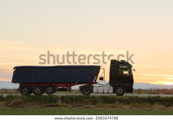 Semi-truck with tipping cargo trailer\
transporting sand from quarry driving on highway hauling goods in\
evening. Delivery transportation and logistics\
concept