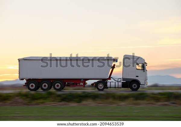 Semi-truck with tipping cargo trailer
transporting sand from quarry driving on highway hauling goods in
evening. Delivery transportation and logistics
concept