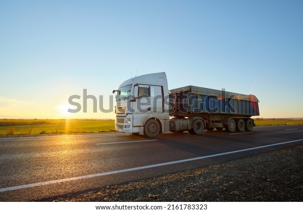 Semi-truck with tipping cargo trailer\
transporting sand from quarry driving on highway hauling goods in\
evening. Delivery transportation and logistics\
concept