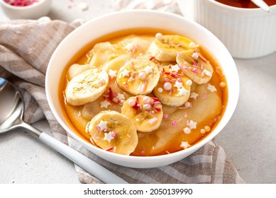 Semolina Porridge With Syrup And Banana. Sweet Breakfast, Baby Food. Semolina Porridge In A White Bowl On A Gray Concrete Background.