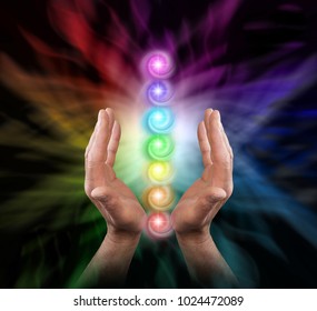 Sending Chakra Healing Energy - Male parallel hands facing upwards against a multicoloured background of energy and the Seven Chakras floating between his hands 