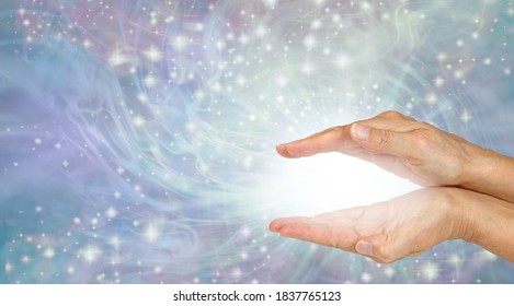 Sending you magical high frequency healing energy - female cupped hands with magical white plasma between flowing sparkles outwards on lilac energy field background with copy space 
