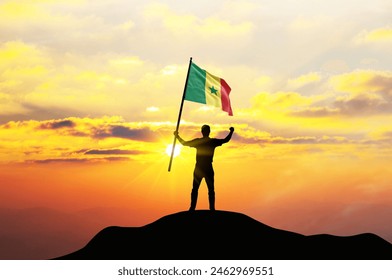 Senegal flag being waved by a man celebrating success at the top of a mountain against sunset or sunrise. Senegal flag for Independence Day. - Powered by Shutterstock