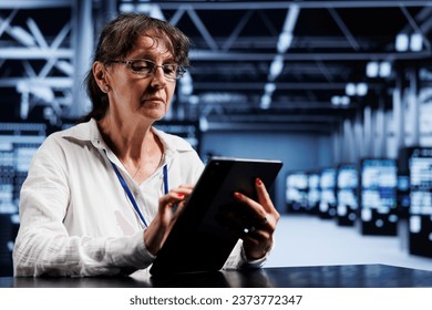 Senescent system administrator using tablet to assess server cybersecurity bugs arising due to unsecured network connections. Skilled mechanic ensuring data center is impenetrable by ddos attacks