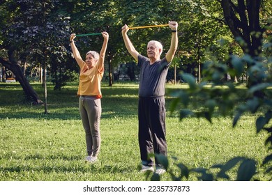 Senior 60 spouses wear sportswear doing hands exercises, training arms outdoor in summer park in the morning using resistance rubber bands. Healthy lifestyle, active retired life use modern appliance - Powered by Shutterstock