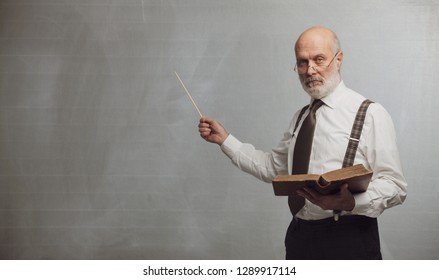 Senior academic professor giving a lecture and pointing at the empty blackboard using a stick: knowledge and traditional education concept - Shutterstock ID 1289917114