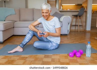 Senior Active Woman Using Smart Phone At Home After Practicing Yoga. The Use Of Technology By The Elderly. Portrait Of Sporty Senior Woman Using Mobile Phone