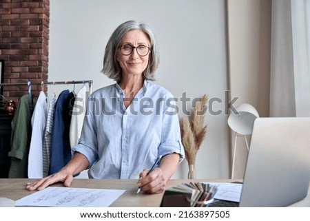 Senior adult 60s aged fashion designer working in showroom design studio. Portrait of sophisticated middle aged confident smiling female designer posing looking in camera.