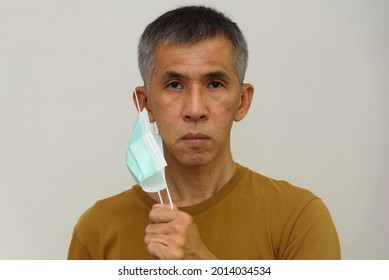 A Senior Adult Asian Man Taking Off Face Mask. Concept Of No Face Mask After Covid-19 Vaccination.