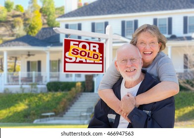 Senior Adult Couple In Front Of Sold Home For Sale Real Estate Sign And Beautiful House.