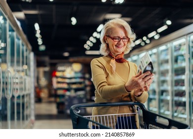 Senior Adult Female Is Shopping At A Grocery Store. She Is Reading Nutrition Facts On The Label. She Is Shopping Alone.