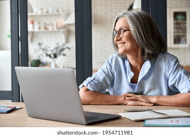 Senior Adult Mid 50s Age Watching At Window At Home Sitting At Table With Laptop. Feeling Happy And Smiling To Thoughts About Future Positive Vision Of Successful Training Career After Learning.