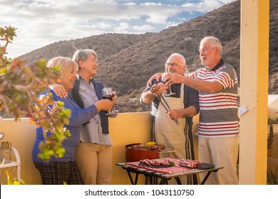 senior adult people group in leisure activity doing barbeque bbq on the rooftop terrace at home with mountain view. meal and wine for two men and two women having fun together under the sunlight - Powered by Shutterstock