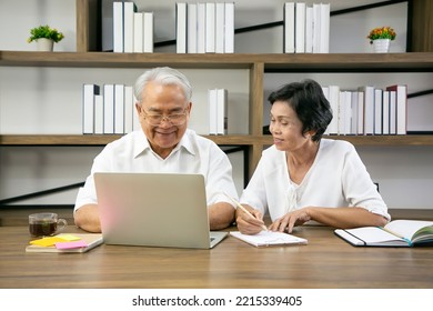 Senior Adult Reading Newspaper Online On Laptop In Livingroom.