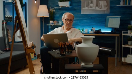 Senior Adult In Wheelchair Using Laptop To Find Artistic Inspiration, Suffering From Chronic Disability Health Condition. Drawing Vase Model On Canvas, Dealing With Physical Impairment.