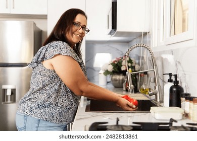 Senior adult woman washing a tomatoes in the sink of the kitchen - Powered by Shutterstock