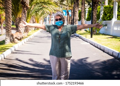 Senior Adult Woman Wearing A Protective Mask Open Arms In The Deserted Street -  Lockdown Due To The Covid-19 Coronavirus. No People Around - Palm Trees