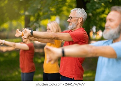 Senior adults participating in stretching exercise, extending their arms forward, elderly men and women making yoga pose, training outdoors in green park, enjoying healthy lifestyle, selective focus - Powered by Shutterstock