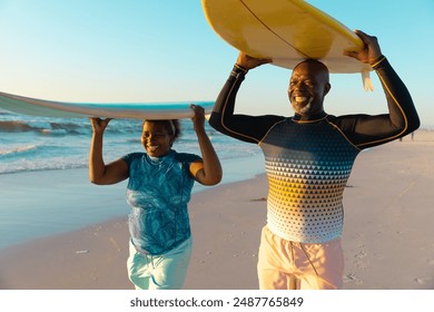 Senior African American couple enjoys a beach day, with copy space. Smiling as they carry a surfboard, they're ready for a fun day in the sun. - Powered by Shutterstock