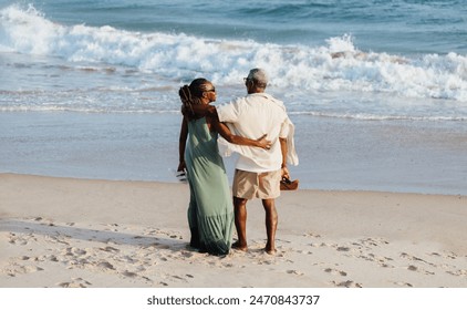 A senior African American couple in a loving embrace walks along a sandy beach, with waves crashing gently in the background, symbolizing enduring love and companionship. - Powered by Shutterstock