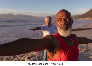 Senior African American Couple Performing Stretching Exercise Together At The Beach. Fitness Yoga And Healthy Lifestyle Concept