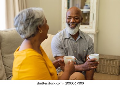 Senior african american couple sitting on sofa drinking coffee in living room. retreat, retirement and happy senior lifestyle concept.