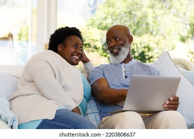 Senior African American Couple Spending Time At Home Together, Sitting On Sofa, Using A Laptop Computer And Smiling. Isolating During Coronavirus Covid 19 Quarantine Lockdown.