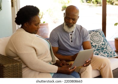 Senior African American Couple Spending Time At Home Together, Sitting On Sofa, Using A Laptop Computer. Isolating During Coronavirus Covid 19 Quarantine Lockdown.