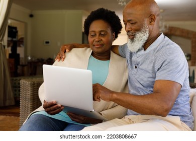 Senior African American Couple Spending Time At Home Together, Sitting On Sofa, Using A Laptop Computer And Embracing. Isolating During Coronavirus Covid 19 Quarantine Lockdown.