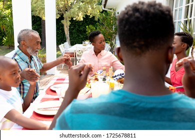 Senior African American Couple And Their Family Spending Time Together In The Garden On A Sunny Day, Sitting By A Table And Praying Before Eating Lunch.