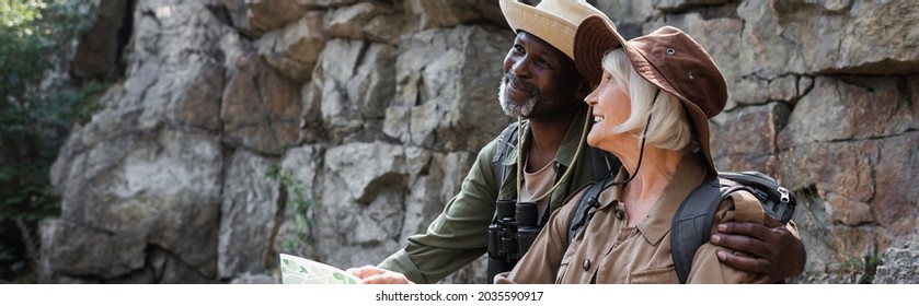 Senior african american hiker hugging smiling wife with map near rock, banner