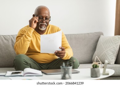 Senior African American Male Working With Papers Wearing Eyeglasses Sitting On Couch At Home. Professional Freelancer Doing Paperwork. Freelance Career Concept. Selective Focus