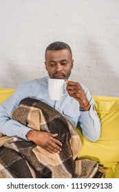 Senior African American Man Drinking Tea While Sitting On Sofa With Plaid