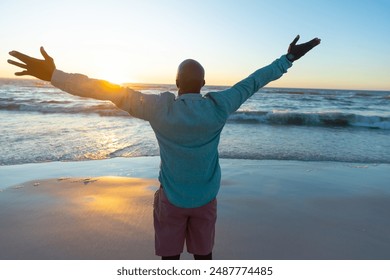 Senior African American man enjoys sunrise at the beach, with copy space. Arms wide open, he embraces the new day with positivity and peace. - Powered by Shutterstock