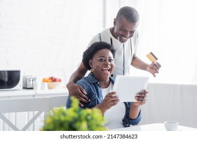 senior african american man holding credit card near amazed wife with digital tablet - Powered by Shutterstock