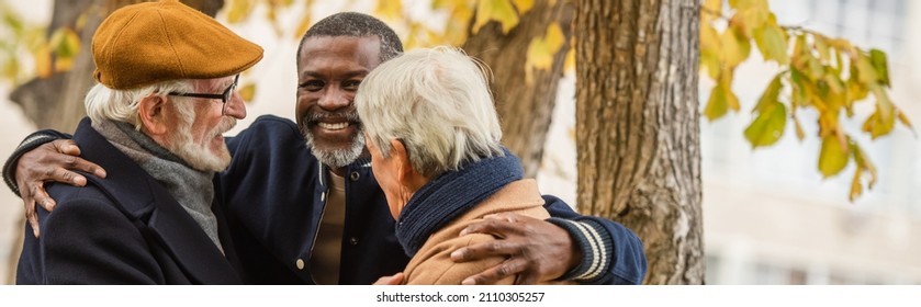 Senior african american man hugging multiethnic friends in autumn park, banner