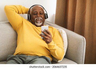Senior African American Man Listening To Music On Smartphone Sitting On Couch At Home. Male Wearing Headphones Enjoying Favorite Song Or Audiobook On Weekend. People And Gadgets - Shutterstock ID 2064637235