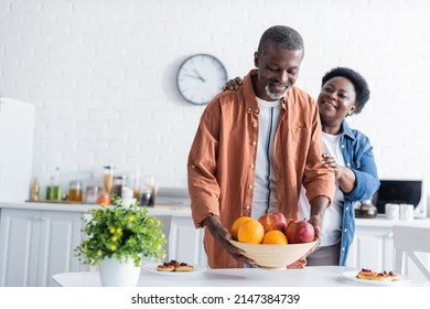 senior african american man putting bowl with fruits on breakfast table near smiling wife - Powered by Shutterstock