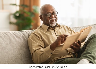 Senior African American Man Reading Book Sitting On Couch At Home, Wearing Eyeglasses. Retired Male Enjoying Reading New Novel Or Business Literature On Weekend. Retirement Leisure Concept - Shutterstock ID 2079163267