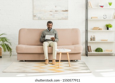 senior african american man sitting on sofa in living room and using digital tablet - Powered by Shutterstock