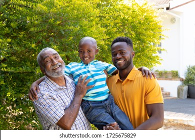 Senior African American man spending time with his son and his grandson in the garden on a sunny day, smiling and looking straight into a camera.