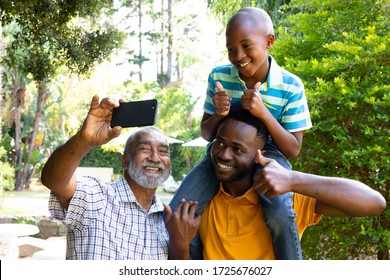 Senior African American man spending time with his son and his grandson in the garden on a sunny day, taking a selfie with a smartphone. - Powered by Shutterstock