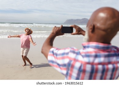 Senior African American Man Taking A Picture Of His Wife On The Beach. Travel Vacation Retirement Lifestyle Concept