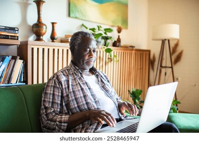 Senior African American man using laptop on couch at home - Powered by Shutterstock