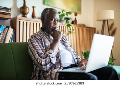 Senior African American man using laptop on couch at home - Powered by Shutterstock