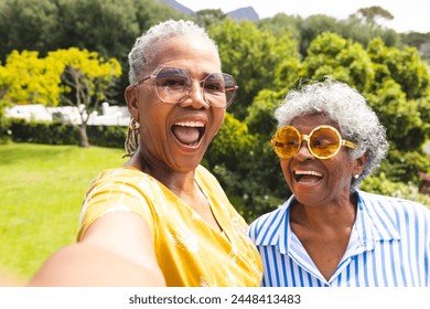 Senior African American woman and senior biracial woman share a joyful moment outdoors. Both are wearing vibrant glasses and bright smiles, capturing a sense of friendship and happiness. - Powered by Shutterstock