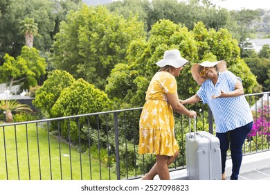 Senior African American woman and biracial woman share a laugh outdoors on vacation with copy space. Dressed in summer attire, they enjoy a moment together on a balcony surrounded by lush greenery. - Powered by Shutterstock