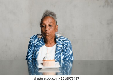 Senior African American woman blowing a candle on a cake on her birthday celebration. A Cheerful elderly woman celebrating her birthday and feeling happy. Birthday celebration concept. - Powered by Shutterstock